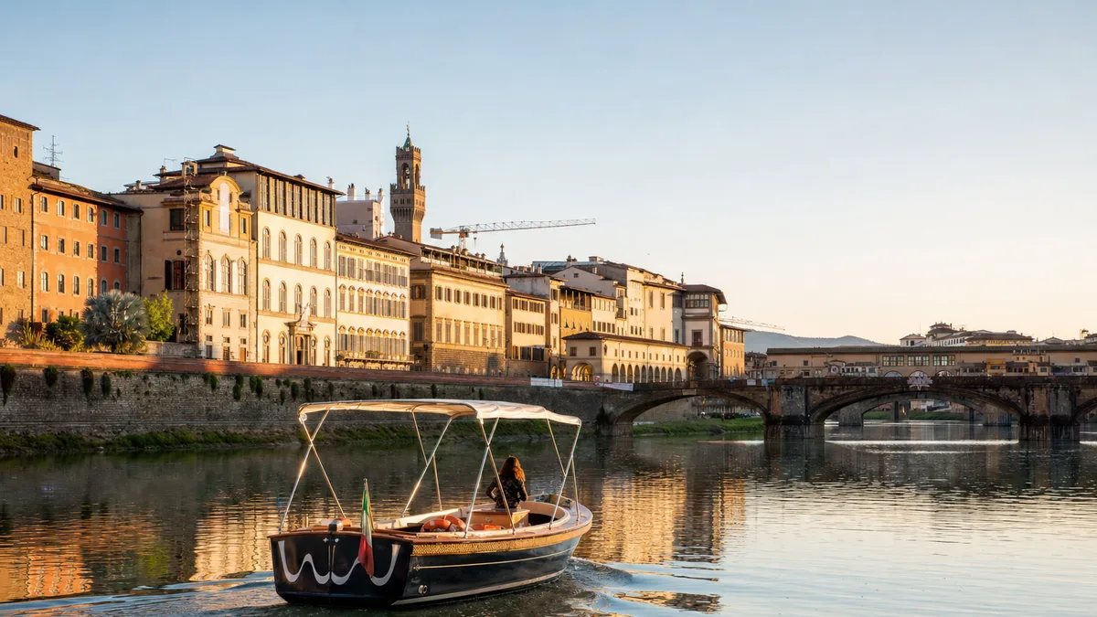 Arno Boat Tour: a small sightseeing boat on the water in Florence, Italy, with the city's real waterfront behind it